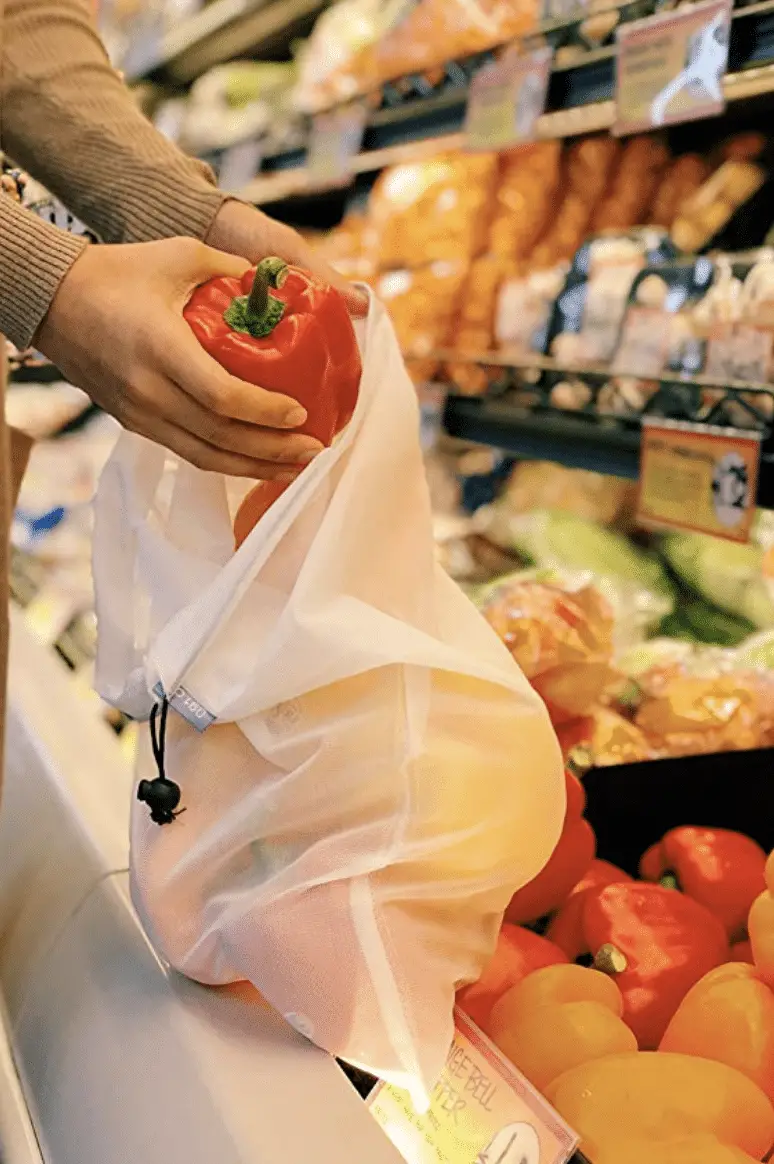 Hands bagging vegetables using a mesh reusable produce bag