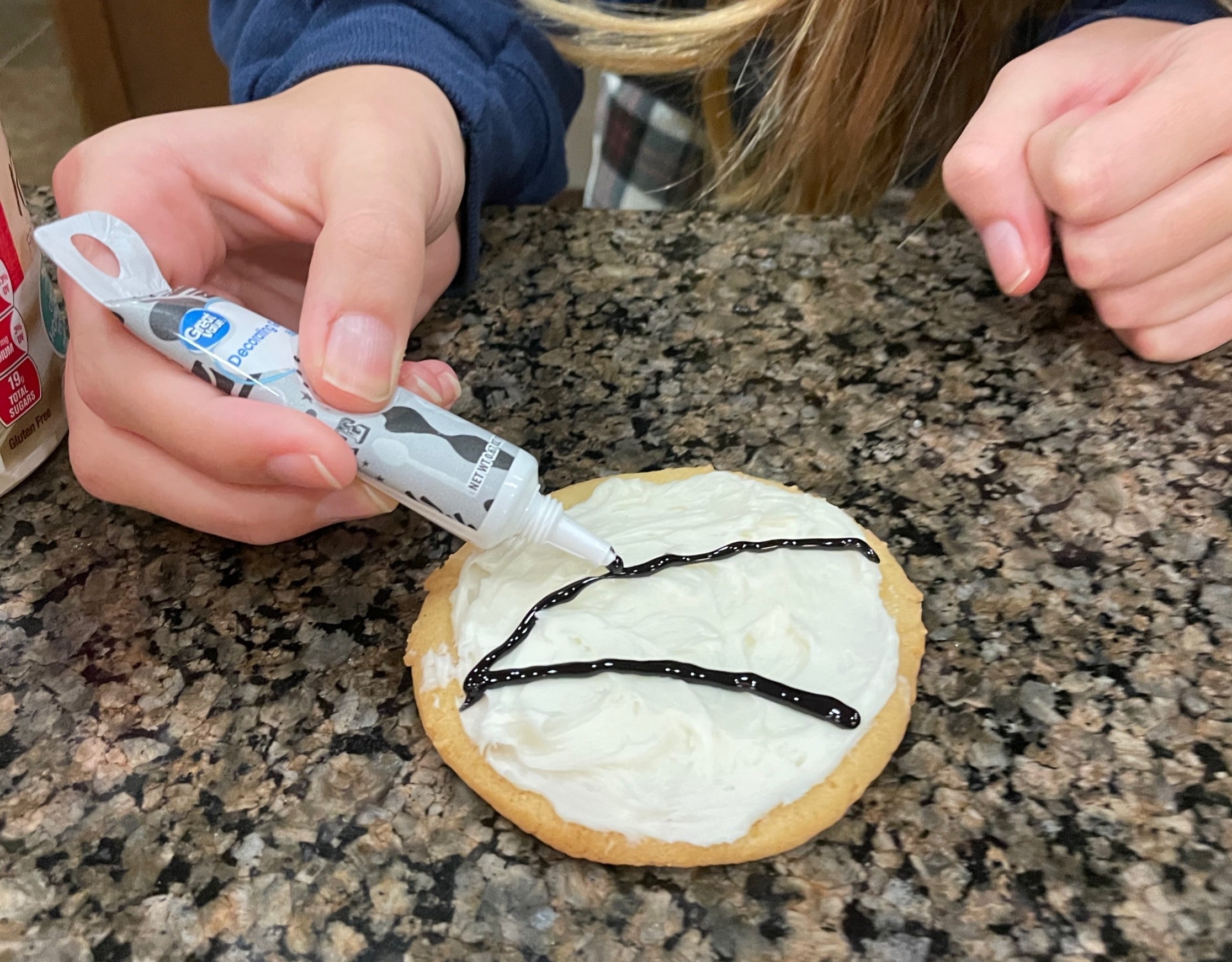 hands decorating a cookie with black icing
