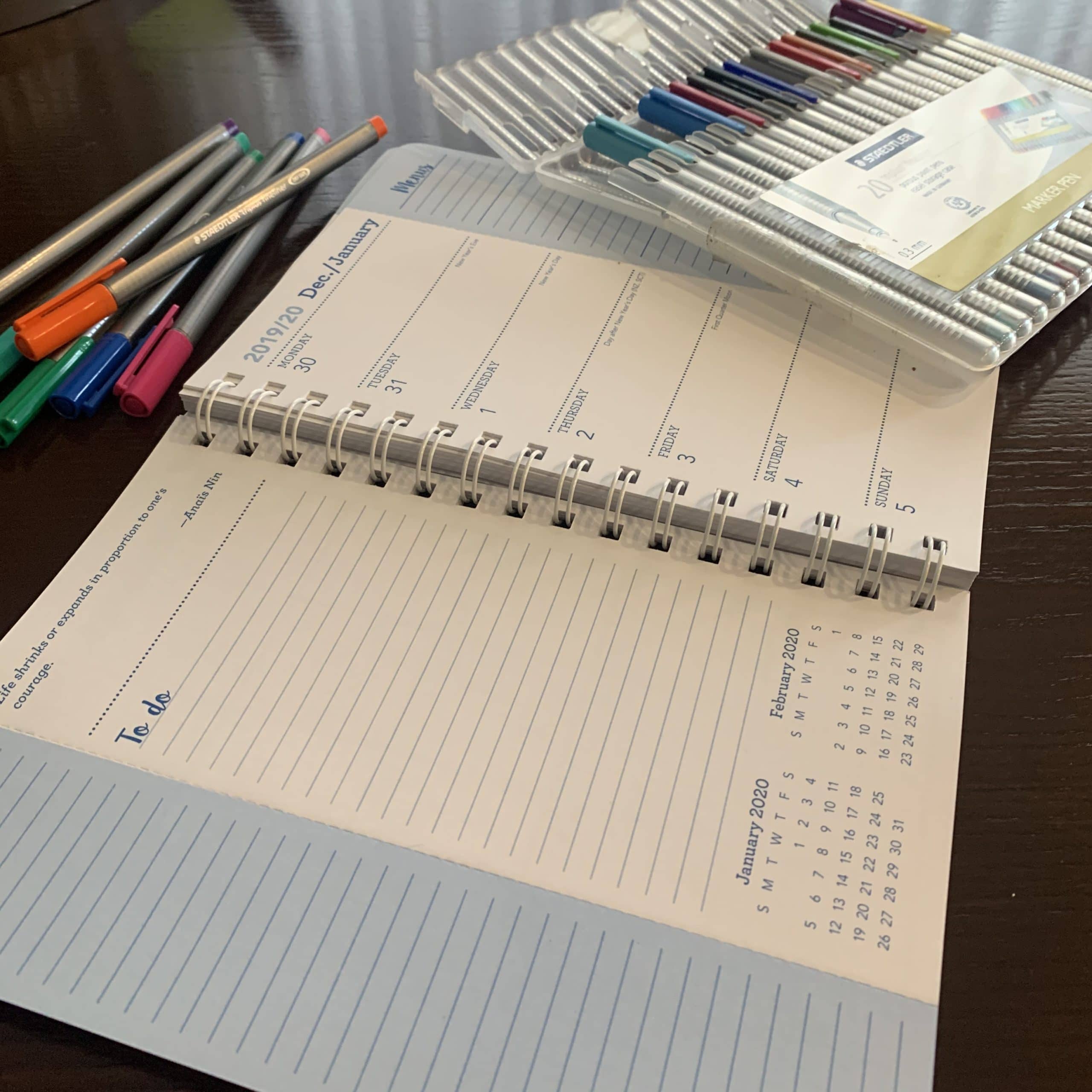 table with empty planner and colorful pens