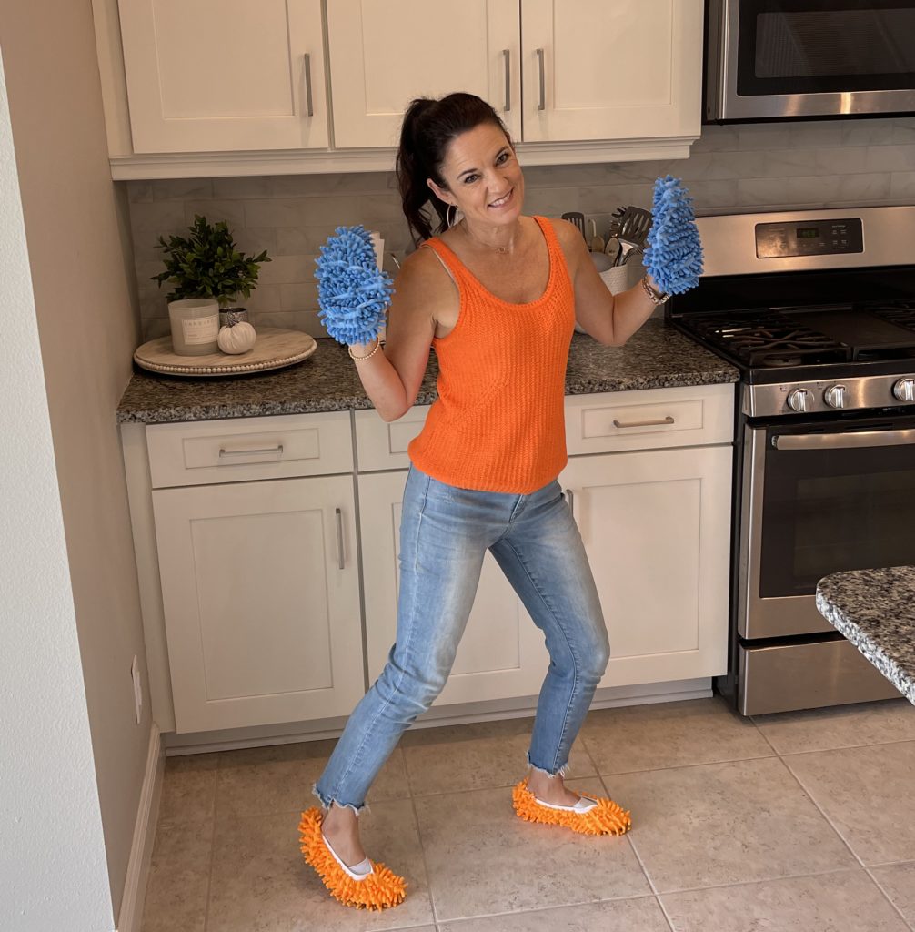 Woman in orange shirt dancing with dusting slippers on